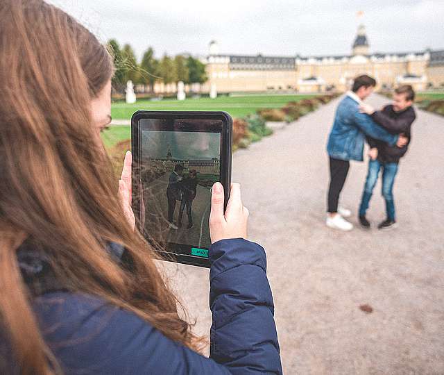Zwei Jugendliche vor dem Karlsruher Schloss. Eine Jugendliche filmt die beiden mit einem Tablet.