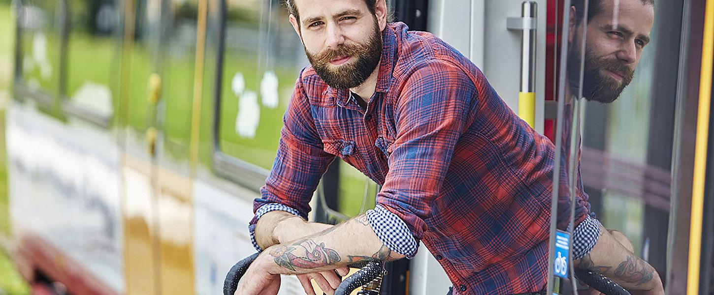 Ein junger Mann in karriertem Hemd lehnt sich aus einer Bahn heraus auf ein Fahrrad.
