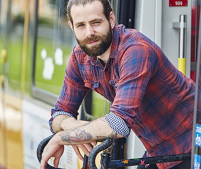 Ein junger Mann in karriertem Hemd lehnt sich aus einer Bahn heraus auf ein Fahrrad.