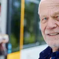 Ein älterer Mann steht an einer Bahnhaltestelle. Verschwommen im Hintergrudn erkennt man eine Frau beim aussteigen aus der Bahn.