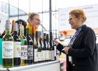 Zwei Besucher*innen stehen an einem Messe-Stand bei der "Eurovino" und verköstigen Weine.