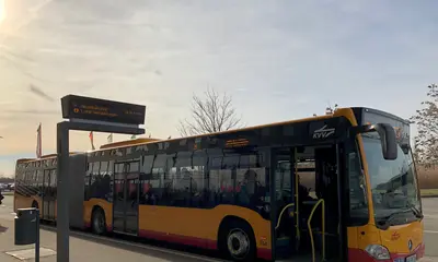 Ein Bus steht mit geöffneten Vordertüren an einer Haltestelle. 