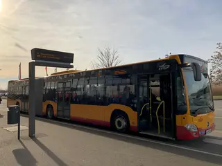 Ein Bus steht mit geöffneten Vordertüren an einer Haltestelle. 