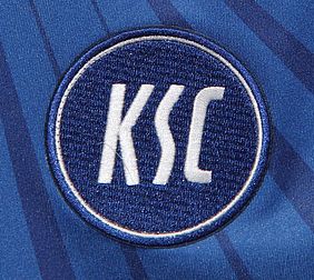 Der Bildausschnitt zeigt das blau-weiße Wappen des Karlsruher SC, aufgenäht auf einem blauen Trikot