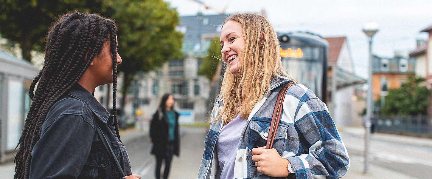 Zwei Teenager-Mädchen unterhalten sich an einer Bahnhaltestelle.
