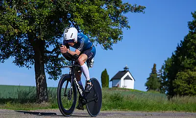 Ein Teilnehmer des Ironman Kraichgau fährt auf einem Rennrad. Im Bildhintergrund sind ein Baum und eine weiße Kapelle zu sehen.