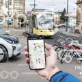 Hand mit Smartphone. Im Hintergrund Auto, Fahrräder und Bahn zu sehen. 