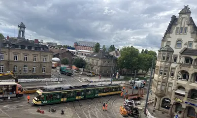 Eine Trambahn passiert bei einer Testfahrt das erneuerte Gleisviereck an der Tullastraße. Im Hintergrund sind das Schlachthof-Areal und das Schloss Gottesaue zu sehen.