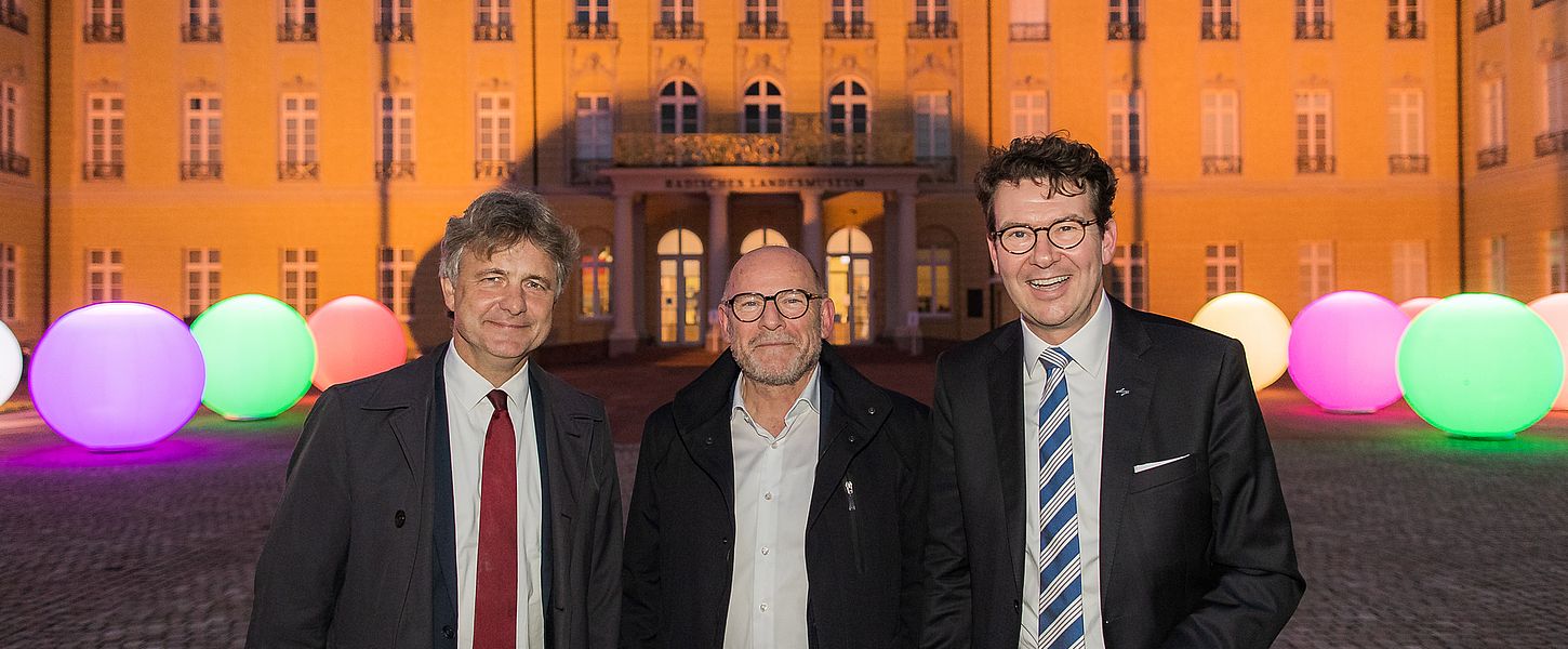Drei Männer in Anzügen stehen vor dem Karlsruher Schloss