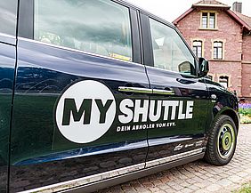 Beifahrertür eines schwarzen "MyShuttle"-Fahrzeuges mit dem Logo des On-Demand-Dienstes.