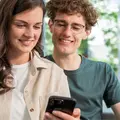 Eine junge Frau und ein junger Mann sitzen in der Bahn und schauen auf ein Smartphone.