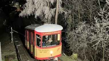 Ein historischer Wagen der Durlacher Turmbergbahn auf einer der letzten Fahrten am Abend des 29. Dezembers 2024. Neben der Bahntrasse stehen Bäume, die mit Raureif bedeckt sind.