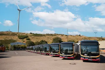 Zwölf neue E-Busse stehen in den VBK-typischen Farben gelb und rot vor einem Windrad. 