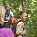 Eine Wandergruppe im Wald. Eine Frau mit Rucksack schaut lächelnd über ihre Schulter nach hinten.