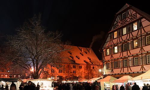 Stände und Besucher beim Weihnachtsmarkt im Kloster Maulbronn bei Nacht.