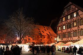 Stände und Besucher beim Weihnachtsmarkt im Kloster Maulbronn bei Nacht.