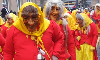 Rot-Gelb gekleidete Narren ziehen mit ihren kunstvollgeschnitzten Holzmasken durch eine Straße