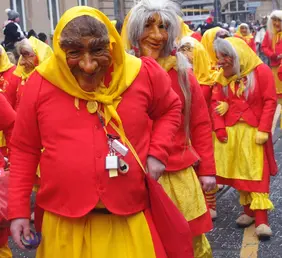 Rot-Gelb gekleidete Narren ziehen mit ihren kunstvollgeschnitzten Holzmasken durch eine Straße