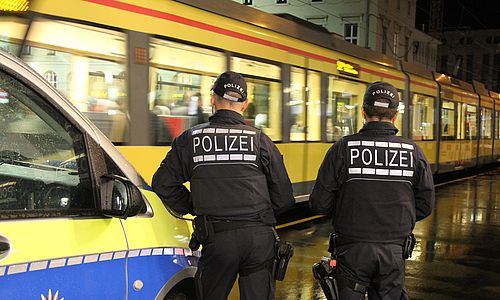 Symbolbild von zwei Polizisten vor einer Stadtbahn. 