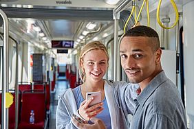 Junge Frau mit Handy in der Hand steht mit jungem Mann in der Bahn 