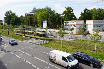 Das Foto zeigt ein Rasengleis in der Kriegsstraße mit einer vorbeifahrenden gelben Trambahn. Im Vordergrund verläuft die Straße für den Autoverkehr.