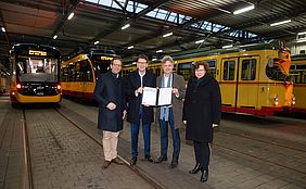 Übergabe des neuen Dienstleistungsbescheids durch Oberbürgermeister Dr. Mentrup an die VBK-Geschäftsführung im Betriebshof Gerwigstraße. Im Hintergrund stehen Straßenbahnen.