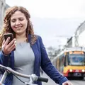 Eine junge Frau schaut lächelnd auf ihr Smartphone. Hinter ihr sieht man eine Bahn.