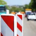 Eine Verkehrsabsperrung an einer Straße. Verschwommen im Hintergrund sieht man ein Auto und einen LKW