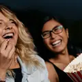 Zwei Frauen sitzen im Kino und essen Popcorn.