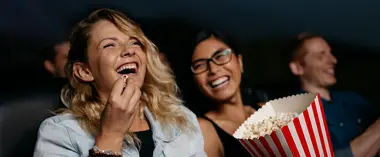 Eine Frau sitzt im Kino, isst Popcorn und lacht. 