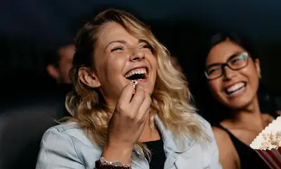 Eine Frau sitzt im Kino, isst Popcorn und lacht. 