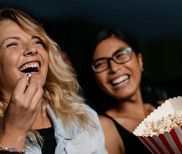 Zwei Frauen sitzen im Kino und essen Popcorn.