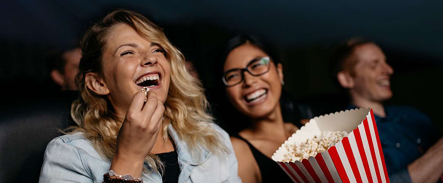 Zwei Frauen sitzen im Kino und essen Popcorn.