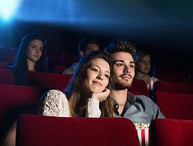 Eine Frau und ein Mann sitzen in einem Kino und schauen gemeinsam einen Film an.