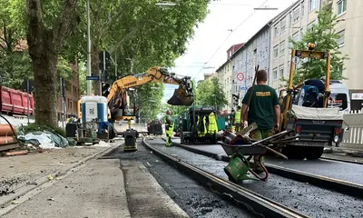 Baustellen-Szenerie mit Bagger und Bauarbeitern. Eine Schubkarre steht links im Vordergrund.