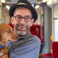Ein Mann mit Hut und Bart in einer Bahn hält einen Hund auf dem Arm.