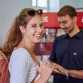 Eine Frau lächelt in die Kamera und im Hintergrund steht ein KVV Mitarbeiter 
