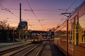 AVG-Stadtbahn fährt bei Sonnenuntergang in der Nähe vom Rheinhafen.