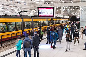 Menschen stehen an einem bahnsteig des Karlsruher Stadtbahntunnels. Eine Straßenbahn fährt die Haltestelle ein.