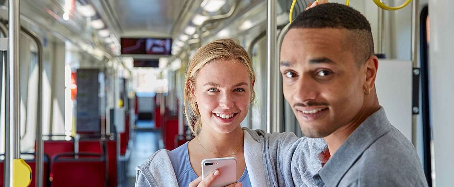 Eine junge Frau und ein junger Mann stehen mit Handy in der Bahn.