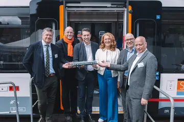 Eine Gruppe von Menschen steht vor einer Tür des VDV-TramTrain mit einem Modell der Bahn. 