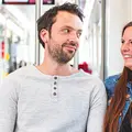 Frau steht lächelnd an einer Bahnhaltestelle.