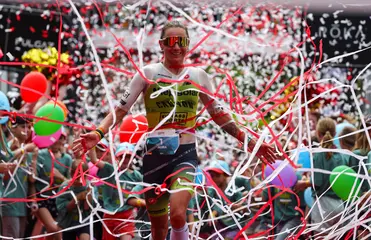 Eine Sportlerin überquert die Ziellinie beim Ironman Kraichgau. Luftschlangen wirbeln durch die Luft.