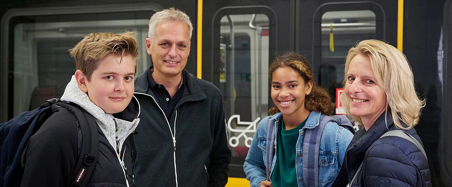 Eine junge Frau sitzt in der Bahn und zieht aus ihrer Einkaufstüte einen Schal. Verschwommen im Vordergrund sieht man zwei Menschen, die sich lachend unterhalten.