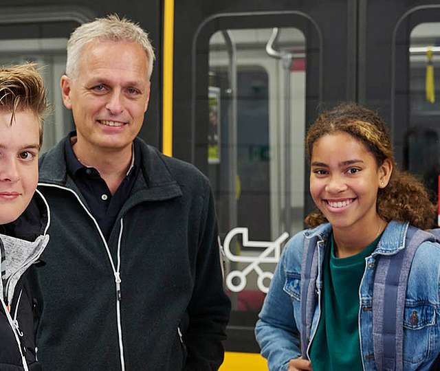 Eine junge Frau sitzt in der Bahn und zieht aus ihrer Einkaufstüte einen Schal. Verschwommen im Vordergrund sieht man zwei Menschen, die sich lachend unterhalten.