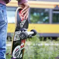 Ein junger Mann, mit der Rückseite zum Betrachter gewandt, hält ein Skateboard in der rechten Hand und schaut vom Gleissteg aus auf die vor ihm stehende gelbe KVV-Bahn.