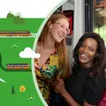 Zwei Frauen befinden sich in der Bahn und lächeln fröhlich in die Kamera.
