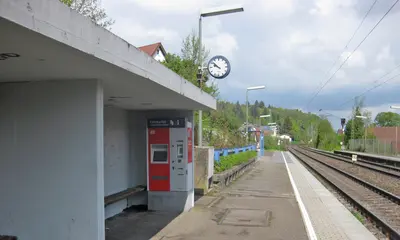 Der Bahnsteig am Haltepunkt Bilfingen: In der Wartehalle in der linken Bildhälfte ist ein Fahrkartenautomat zu sehen. Am rechten Bildrand verlaufen die Gleise der Bahnstrecke. Der Himmel ist bewölkt.