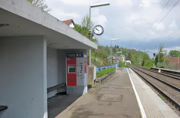 Ein Foto zeigt den Haltepunkt Bilfingen mit Wartehäuschen, Fahrkartenautomat und einer Uhr. 