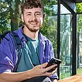 Ein junger Mann sitzt lächelnd an der Haltestelle und hält sein Smartphone.